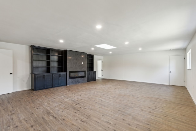 unfurnished living room featuring a skylight, a large fireplace, built in shelves, and light wood-type flooring