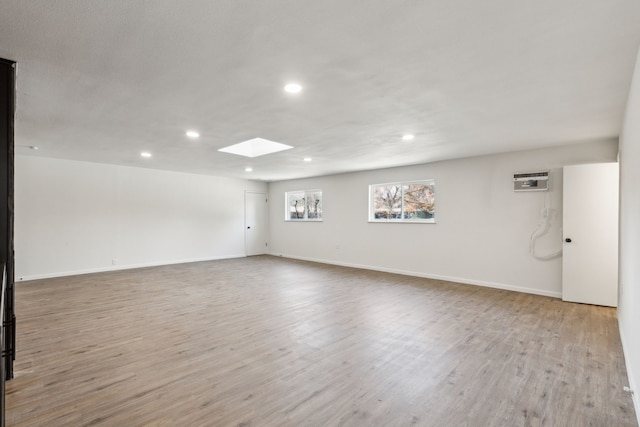 unfurnished room featuring light wood-type flooring, a wall unit AC, and a skylight