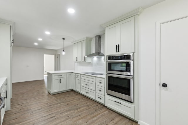 kitchen featuring wall chimney exhaust hood, decorative backsplash, double oven, decorative light fixtures, and kitchen peninsula