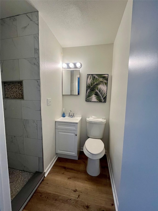 bathroom with hardwood / wood-style floors, vanity, toilet, a textured ceiling, and a tile shower