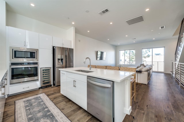 kitchen with sink, wine cooler, an island with sink, white cabinetry, and stainless steel appliances