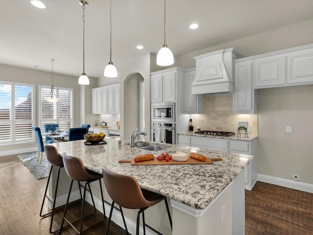 kitchen featuring white cabinets, a large island with sink, stainless steel appliances, and premium range hood