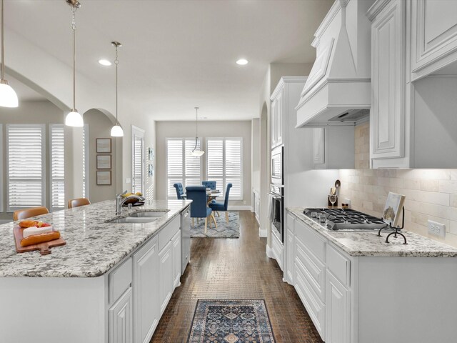 kitchen featuring white cabinets, decorative light fixtures, custom range hood, and sink