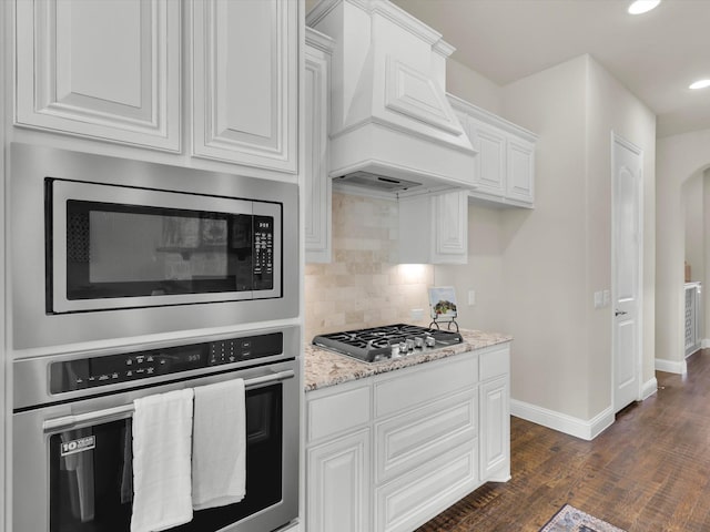 kitchen featuring white cabinetry, light stone countertops, stainless steel appliances, dark hardwood / wood-style flooring, and premium range hood