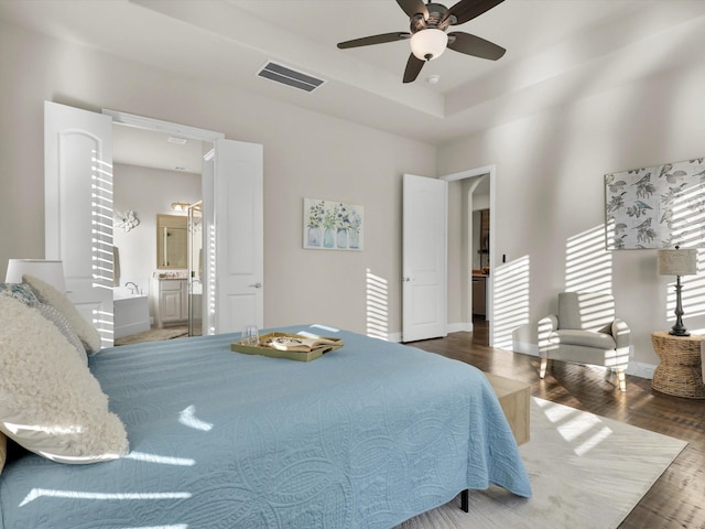 bedroom featuring hardwood / wood-style flooring, ceiling fan, ensuite bathroom, and a tray ceiling