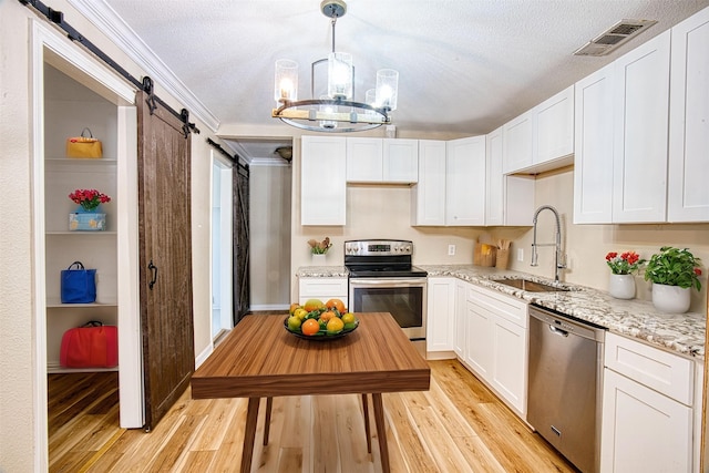 kitchen with white cabinetry, a barn door, appliances with stainless steel finishes, light stone countertops, and sink