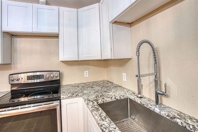 kitchen with stainless steel electric range oven, sink, and white cabinetry