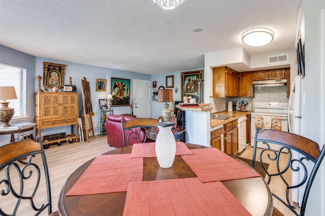 dining room featuring sink, a textured ceiling, and light wood-type flooring