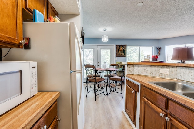 kitchen featuring butcher block counters, light hardwood / wood-style floors, decorative backsplash, decorative light fixtures, and french doors