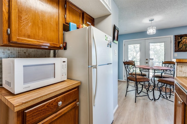 kitchen featuring pendant lighting, white appliances, light hardwood / wood-style floors, a textured ceiling, and french doors