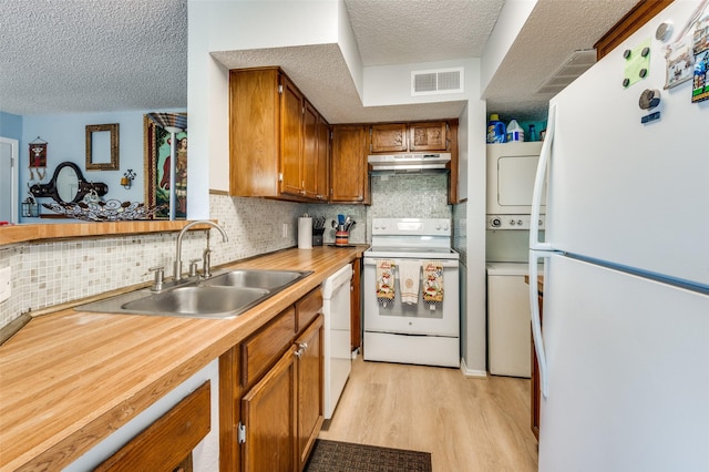 kitchen featuring sink, light wood-type flooring, stacked washer / drying machine, white appliances, and a textured ceiling