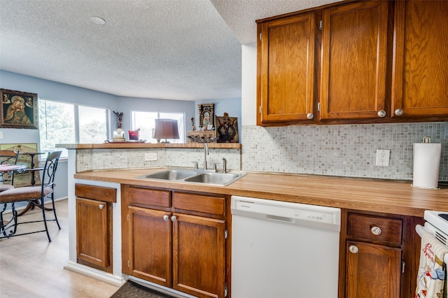 kitchen with sink, dishwasher, kitchen peninsula, light hardwood / wood-style floors, and backsplash