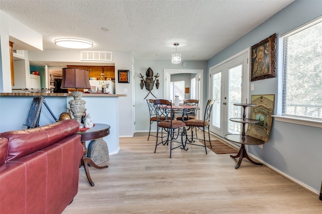 dining room featuring french doors, light hardwood / wood-style flooring, and a textured ceiling