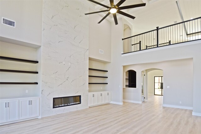 unfurnished living room with built in shelves, a premium fireplace, a towering ceiling, and light hardwood / wood-style floors