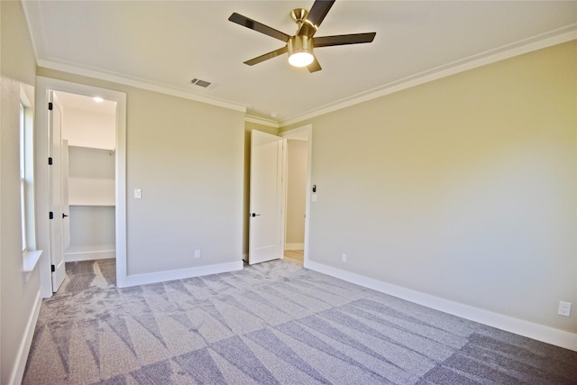 unfurnished bedroom featuring ceiling fan, a walk in closet, light carpet, a closet, and ornamental molding