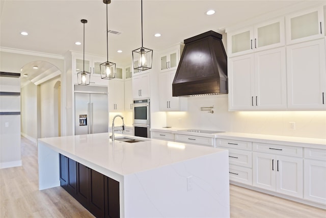 kitchen featuring appliances with stainless steel finishes, custom exhaust hood, a kitchen island with sink, sink, and white cabinets