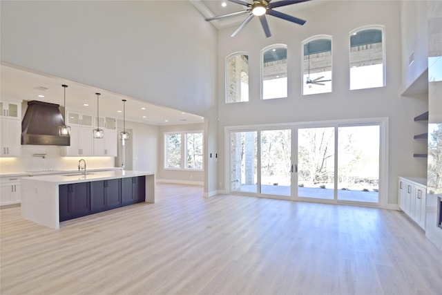 kitchen with premium range hood, ceiling fan, a kitchen island with sink, pendant lighting, and light hardwood / wood-style flooring