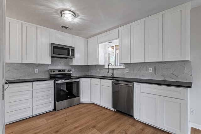 kitchen with appliances with stainless steel finishes, sink, backsplash, white cabinets, and light wood-type flooring