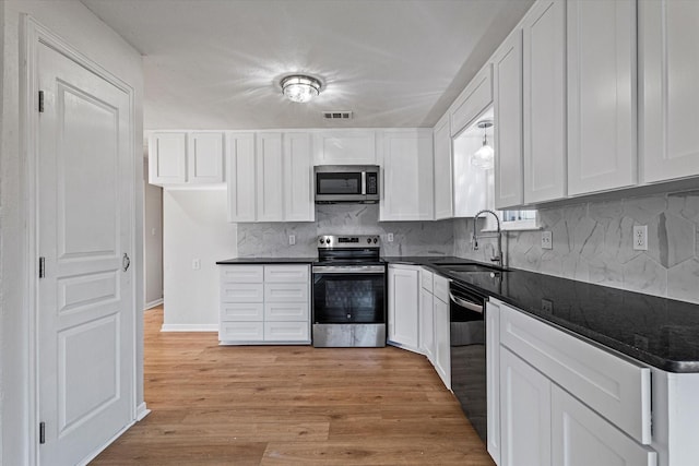 kitchen with appliances with stainless steel finishes, sink, white cabinets, decorative backsplash, and light hardwood / wood-style floors