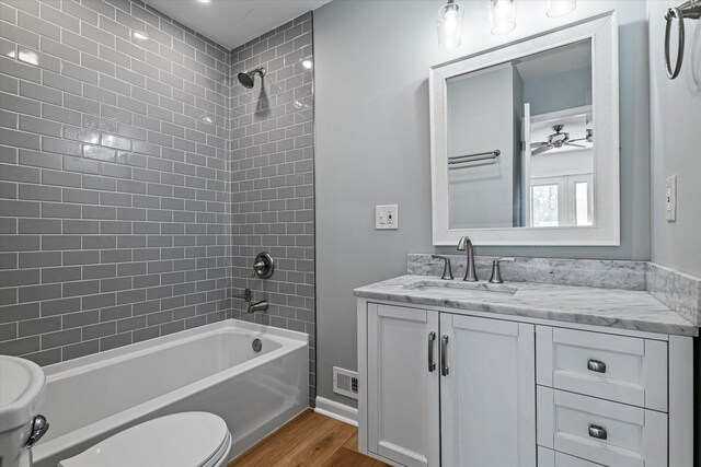 full bathroom with tiled shower / bath, wood-type flooring, vanity, ceiling fan, and toilet