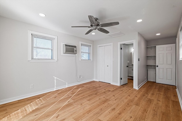 unfurnished bedroom featuring ceiling fan, connected bathroom, a wall unit AC, and light hardwood / wood-style flooring