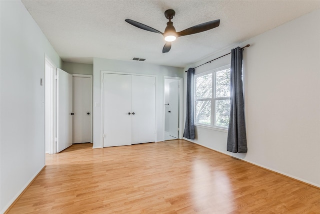 unfurnished bedroom featuring a textured ceiling, ceiling fan, light hardwood / wood-style flooring, and multiple closets