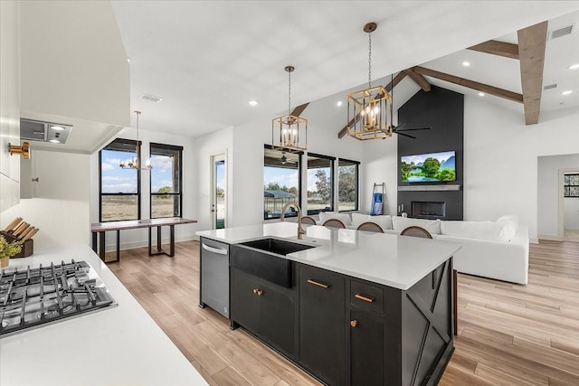 kitchen featuring ceiling fan with notable chandelier, sink, a center island with sink, a fireplace, and hanging light fixtures