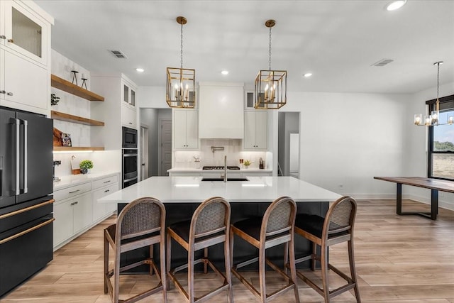 kitchen with high end refrigerator, a kitchen island with sink, decorative light fixtures, white cabinetry, and oven