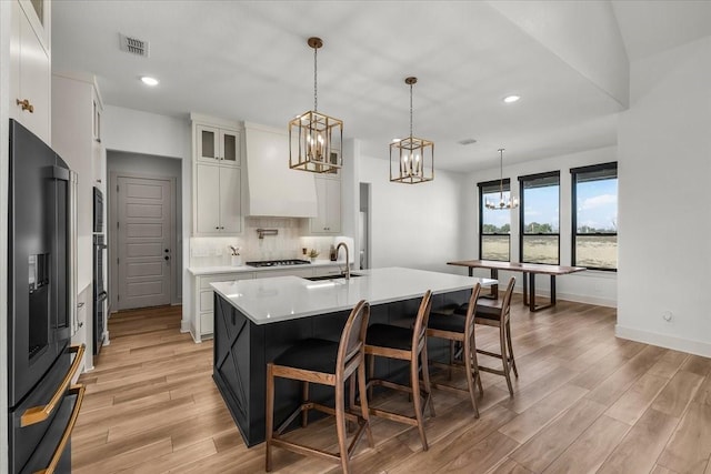 kitchen with stainless steel fridge, a kitchen island with sink, pendant lighting, light hardwood / wood-style floors, and white cabinetry