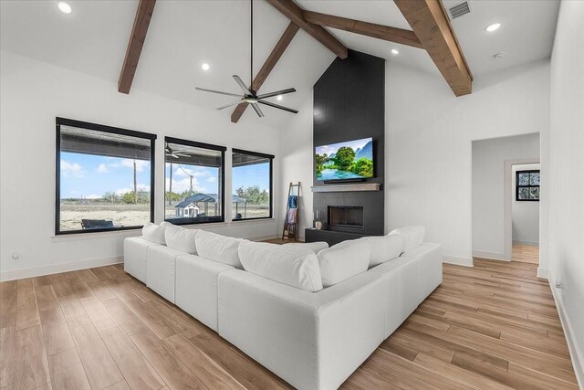 living room with ceiling fan, a fireplace, beamed ceiling, and high vaulted ceiling