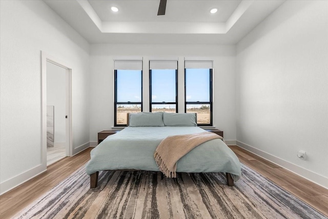 bedroom featuring a raised ceiling, ensuite bath, ceiling fan, and wood-type flooring