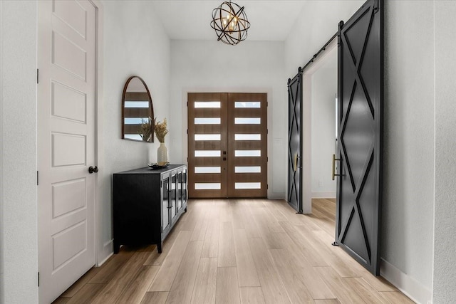 entryway featuring light wood-type flooring, french doors, a barn door, and a chandelier