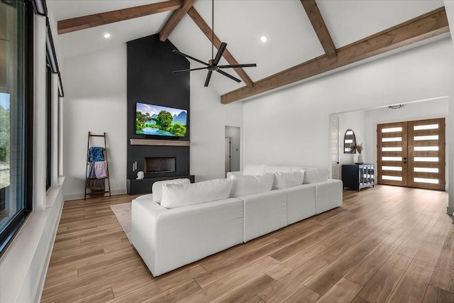 living room featuring a large fireplace, beam ceiling, light wood-type flooring, and french doors