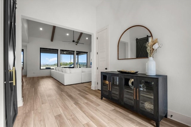 living room with beam ceiling, ceiling fan, a towering ceiling, and light hardwood / wood-style floors