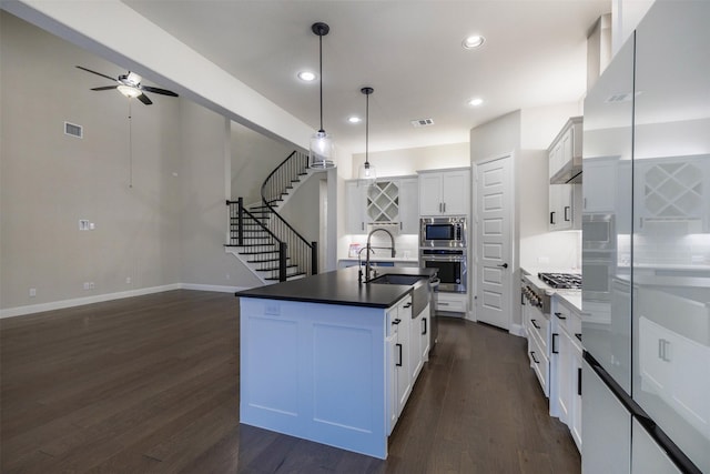 kitchen featuring a kitchen island with sink, backsplash, white cabinets, appliances with stainless steel finishes, and decorative light fixtures