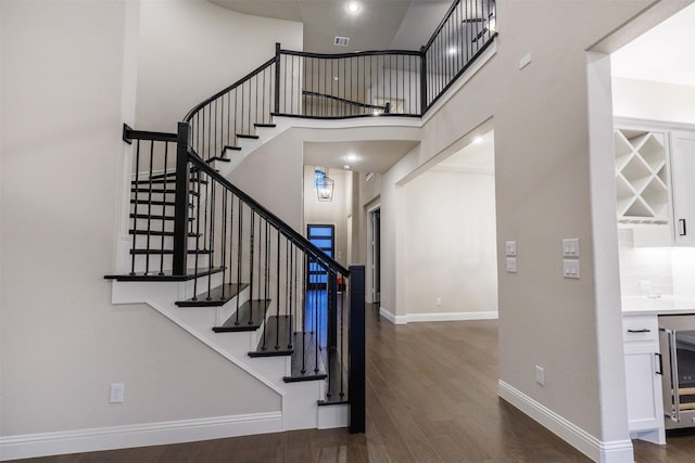 staircase featuring wine cooler, wood-type flooring, and a high ceiling