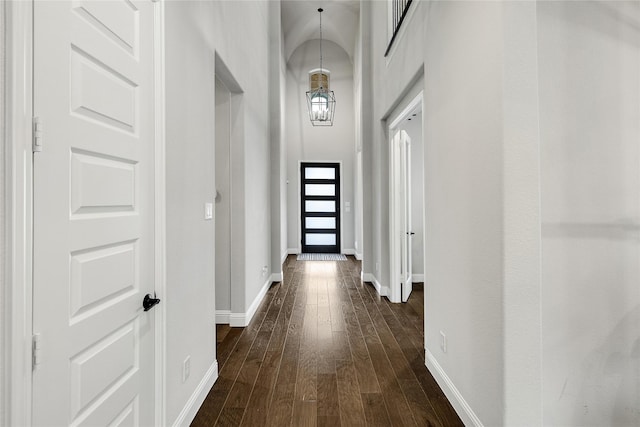 hallway with dark hardwood / wood-style flooring, a towering ceiling, and a chandelier