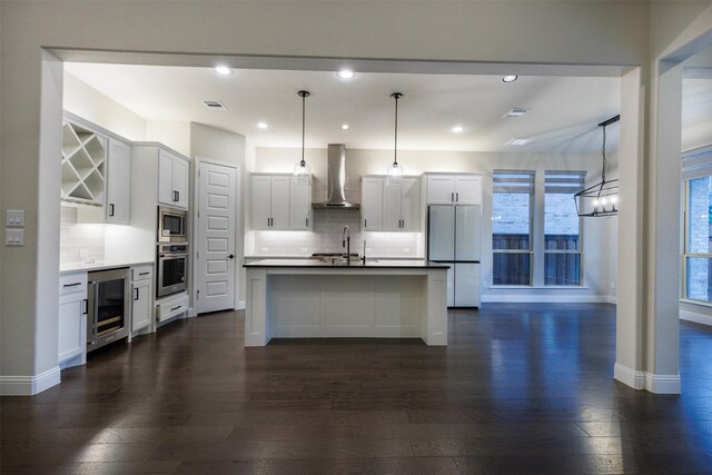 kitchen featuring wall chimney exhaust hood, appliances with stainless steel finishes, decorative light fixtures, white cabinetry, and beverage cooler