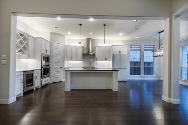 kitchen with decorative light fixtures, white cabinets, wine cooler, stainless steel appliances, and wall chimney exhaust hood