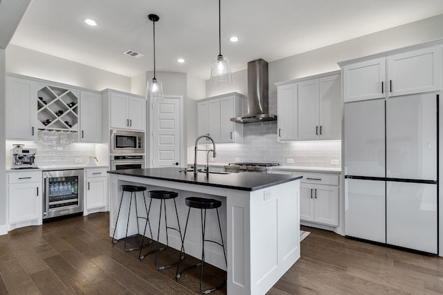 kitchen featuring appliances with stainless steel finishes, wine cooler, white cabinets, a center island with sink, and wall chimney exhaust hood