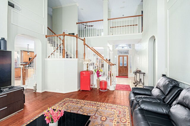 living room featuring a towering ceiling, wood-type flooring, and ornamental molding