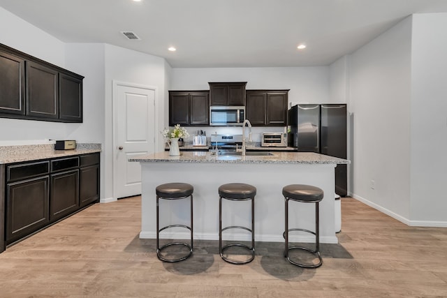 kitchen with light hardwood / wood-style floors, sink, a kitchen island with sink, and appliances with stainless steel finishes