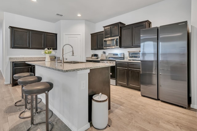 kitchen with sink, light hardwood / wood-style flooring, an island with sink, appliances with stainless steel finishes, and dark brown cabinetry