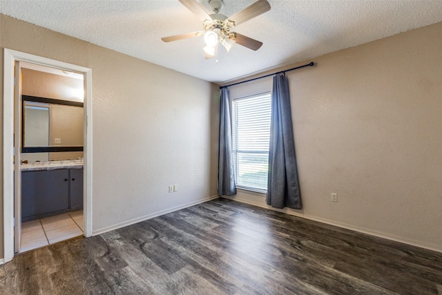 unfurnished bedroom featuring ceiling fan, dark hardwood / wood-style flooring, a textured ceiling, and connected bathroom