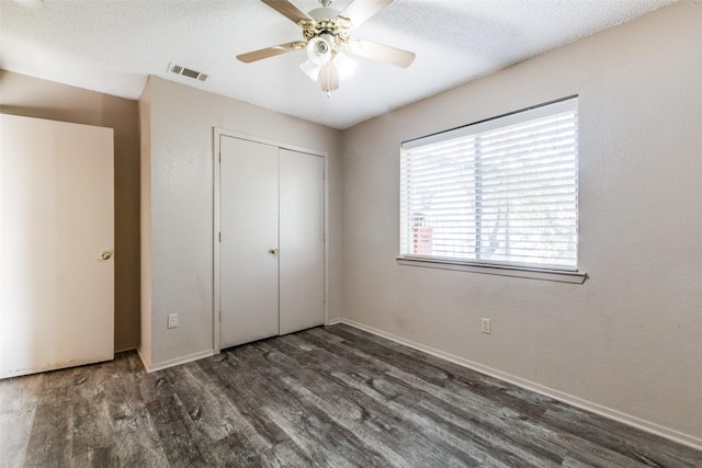 unfurnished bedroom with ceiling fan, dark hardwood / wood-style flooring, a textured ceiling, and a closet