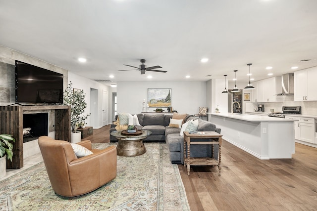 living room with ceiling fan, a fireplace, light wood-type flooring, and sink