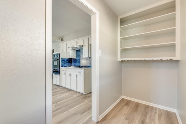 interior space featuring white cabinets, backsplash, stainless steel gas cooktop, and light hardwood / wood-style flooring