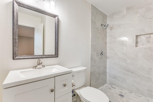 bathroom with a tile shower, vanity, and toilet