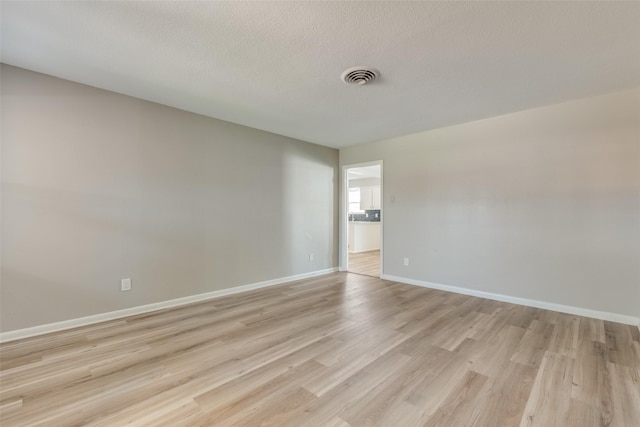 spare room with a textured ceiling, light wood-type flooring, visible vents, and baseboards