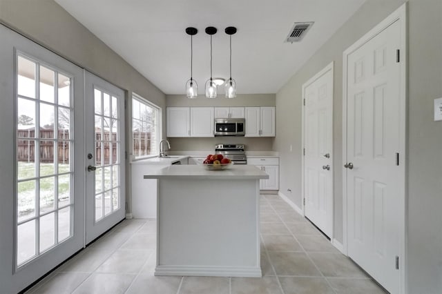 kitchen featuring appliances with stainless steel finishes, hanging light fixtures, french doors, white cabinets, and sink